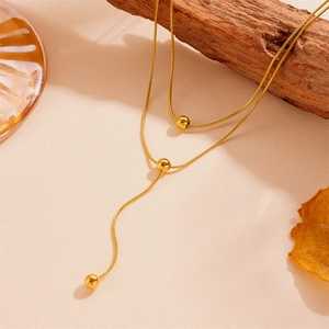 Gros plan détaillé d'un collier double rang en acier inoxydable doré avec pompons perles.