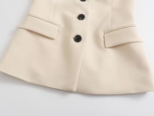 Detailed close-up of beige woven vest showing dark brown buttons and pocket flaps