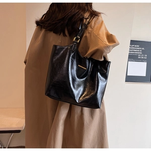 Detail view of a large black soft leather tote bag worn by a model in a trench coat