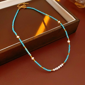 Detail of turquoise and freshwater pearl beaded necklace with gold chain in a display tray