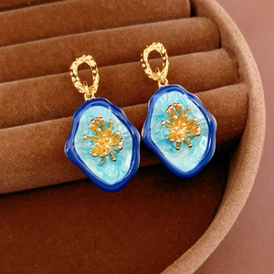 Macro detail of vintage oval flower earrings featuring blue enamel and gold textured rings