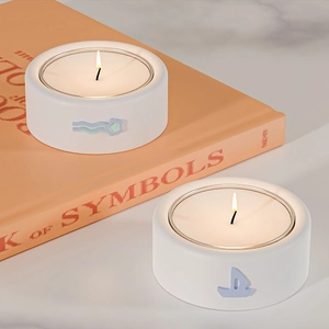 Dettaglio di un portacandele bianco con rilievo a vela su libro arancione e sfondo marmo