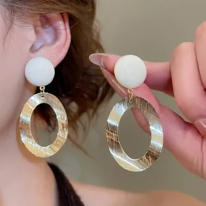 Minimalist oval brushed gold metal earrings with white resin stud on a warm background