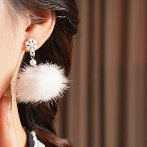Close-up of model wearing winter snowflake earrings with white pompom and pearl accents