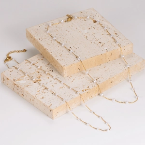 Elegant gold layered necklaces featuring small white pearls on a textured stone display