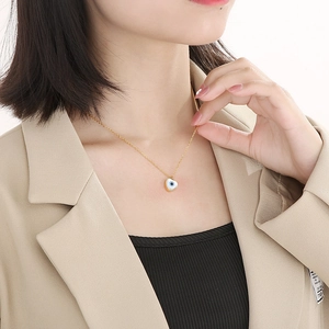 Close-up of a heart-shaped Evil Eye pendant on a gold chain worn by a female model