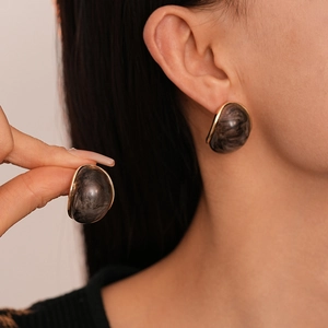 Detail of marble pattern resin earrings with golden metal edges worn by a model