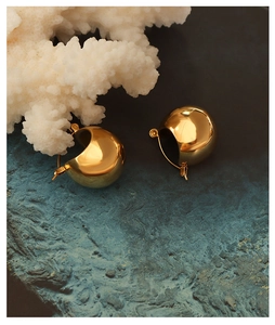 Close-up of golden dome hoop earrings with mirror finish on deep blue rock texture