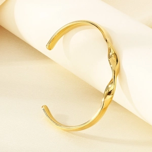 Close-up of 18K gold-plated stainless steel twisted wavy bangle on a minimalist display