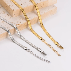 Gold and silver stainless steel flat snake necklaces on beige travertine stone