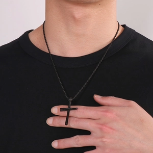 Close-up of a black cross pendant necklace with woven rope chain on a male model