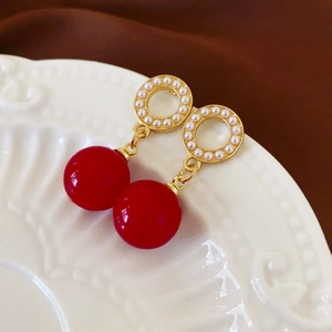 Close-up of vintage red bead earrings with golden pearl-encrusted rings on ceramic