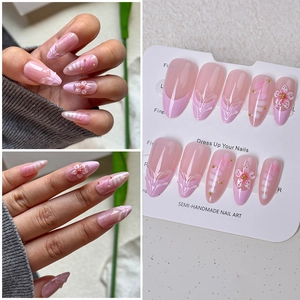 Detail of pink almond press-on nails with 3D white flower carvings and gold beads
