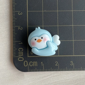 Close-up of a blue resin penguin charm with wings on a measurement mat for DIY crafts