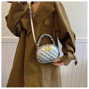 Detail of a silver quilted crossbody bag with a pleated handle worn over a trench coat