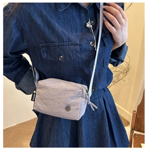 Dettaglio della borsa a tracolla grigia a pieghe con etichetta e logo in metallo su modella