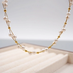 Elegant handmade pearl and gold bead cross-woven necklace displayed on a tray