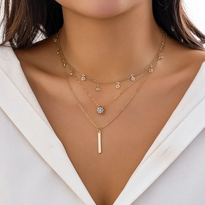 Detail of layered gold necklace with rhinestone flower and metal bar charms on model