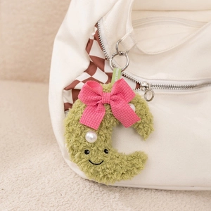 Detailed view of a green plush moon charm with a pink bow hanging on a checkered canvas bag