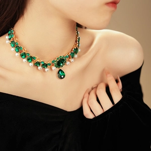 Close-up of vintage necklace with green emerald-cut stones and white pearls on a model