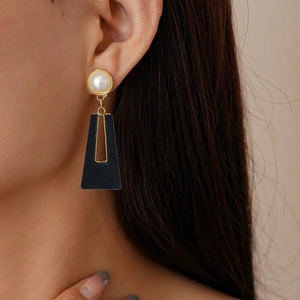 Détail de boucles d'oreilles trapèze noires géométriques avec perle sur modèle