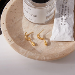 Détail de boucles d'oreilles dorées en goutte avec cristaux dans un bol en pierre