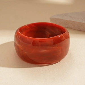 Macro shot of red and amber marbled resin cuff bracelet on beige background with stone