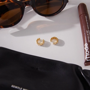 Detail of gold C-shaped earrings with square cubic zirconia on a minimalist background