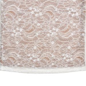 Detailed close-up of intricate white floral lace fabric with delicate scalloped patterns