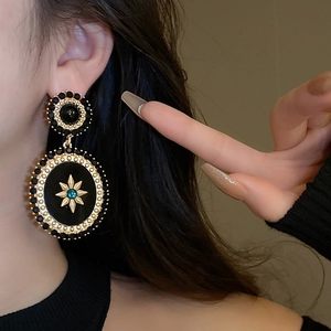 Detail of vintage-style oval pearl earrings with black and gold starburst design on ear