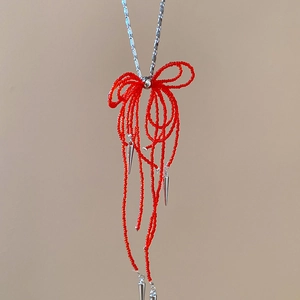 Detail of red beaded bow necklace featuring silver metal tassels and cone pendants