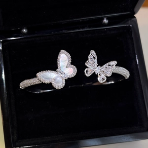 Macro detail of silver-tone open bangle with mother-of-pearl and pavé zircon butterflies