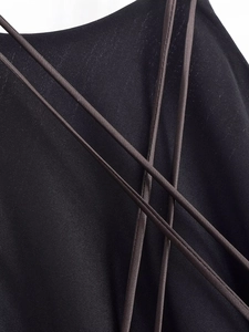 Detail of black fabric dress featuring criss-cross brown lacing with tassel fringe trim