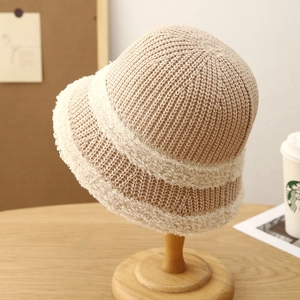 Minimalist beige knitted bucket hat for women with white faux fur trim on a wooden stand