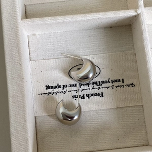 Macro view of polished silver C-shaped crescent stud earrings on a textured fabric surface