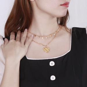 Détail d'un collier double rang doré en titane avec pendentif cœur et étoiles sur mannequin