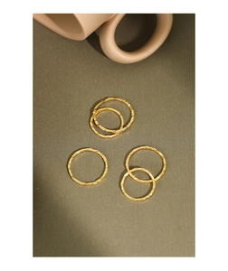 Detail of five-piece gold hammered texture rings on minimalist olive green background