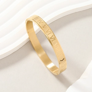 Macro detail of gold stainless steel bangle featuring engraved Roman numerals decoration