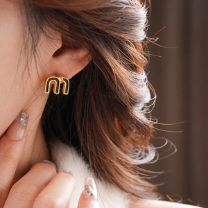 Close-up of model wearing black and gold letter M stud earrings with polished enamel finish
