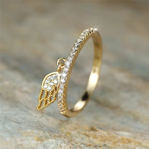 Macro shot of gold-plated ring with sparkling zircon pavé and hanging angel wing pendant