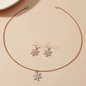 Golden necklace and earrings set featuring white snowflake charms on a beige background