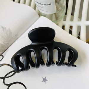 Detailed view of a large matte black flower hair claw clip on a white magazine background