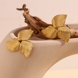 Macro shot of 18K gold clover earrings featuring brushed metal texture on a ceramic vase