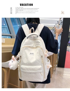 Gros plan du sac à dos blanc texturé avec fermeture éclair argentée et breloque lapin mignon