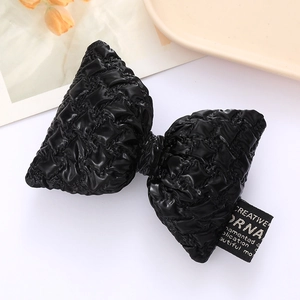 Close-up of a 3D padded black quilted leather bow with a creative ornamental woven label