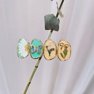 Detailed close-up of handmade oval resin hair clips with dried flowers and butterfly charms