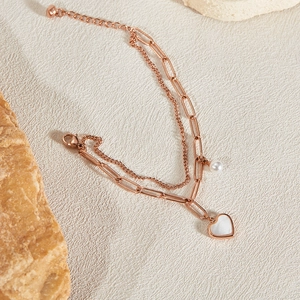 Detail of rose gold double-layer chain bracelet with white heart charm and small pearl
