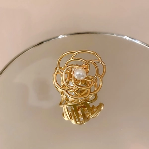 Macro detail of golden metal camellia hair claw with an elegant pearl center on a mirror