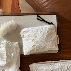 Close-up of white floral lace pouch with simple wish label and textured zipper