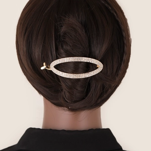 Detail of a golden metal oval hair claw clip with rhinestones worn on a woman's hair